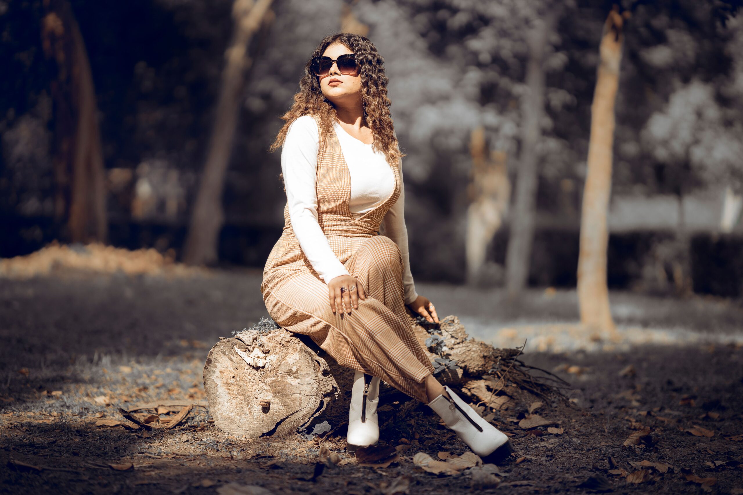 Fashionable woman seated on tree trunk in autumn forest, India